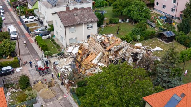 Ein eingestürztes Wohnhaus in einem Wohngebiet mit Einsatzkräften und einem Bagger vor Ort.