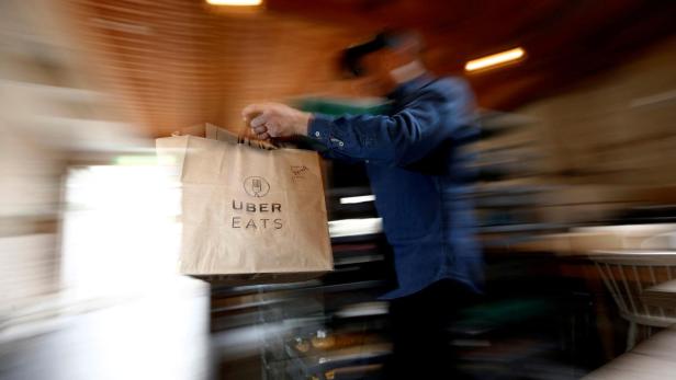 Unscharfer Mann trägt eine Uber-Eats-Tüte in einem Restaurant.