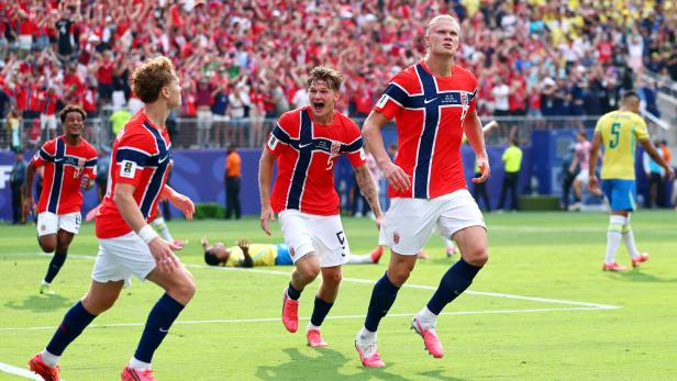 Erling Haaland und seine norwegischen Teamkollegen jubeln nach einem Tor auf dem Fußballfeld vor einer großen Zuschauermenge.