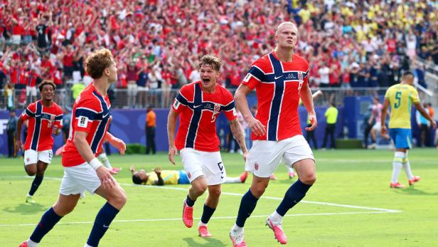 Erling Haaland und seine norwegischen Teamkollegen jubeln nach einem Tor auf dem Fußballfeld vor einer großen Zuschauermenge.