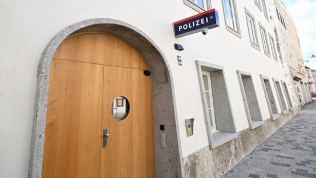 Weiße Gebäudefassade mit Holzportal und Schild „Polizei“ an einer schmalen gepflasterten Straße.