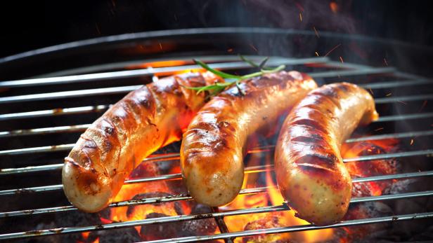 Grilled sausages on grill with smoke and flame