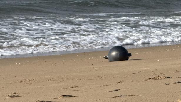 Schwarze Kugel liegt am Strand nahe der Brandung.