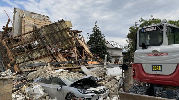 Eingestürztes Haus mit Trümmern, eingeklemmtem Auto und Bagger bei Räumarbeiten.