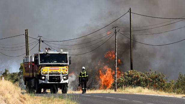Ein Feuerwehrmann steht neben einem Einsatzfahrzeug der Sécurité Civile vor einem brennenden Waldstück mit dichtem Rauch.