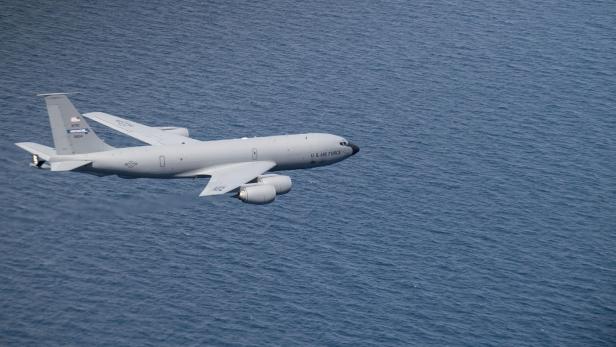 Ein graues Tankflugzeug fliegt über dem blauen Meer