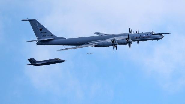Ein russischer Tupolew Tu-142-Aufklärer fliegt vor einem F-35-Kampfjet am blauen Himmel.