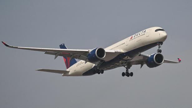 Delta-Passagierflugzeug mit ausgefahrener Fahrwerks, im Steigflug vor grauem Himmel.
