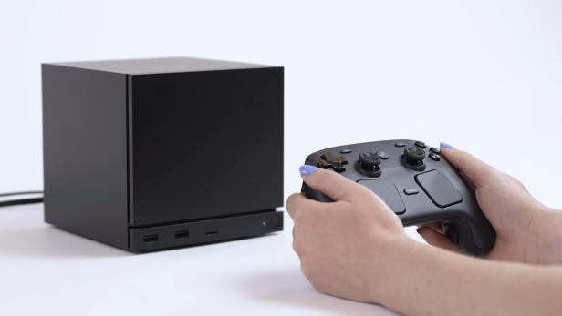 Schwarzer Gaming-PC steht im Hintergrund, eine Frau hält einen Controller im Vordergrund