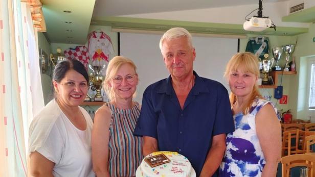 Drei Frauen und ein Mann stehen lächelnd zusammen, während der Mann eine Torte mit der Aufschrift „42“ hält.