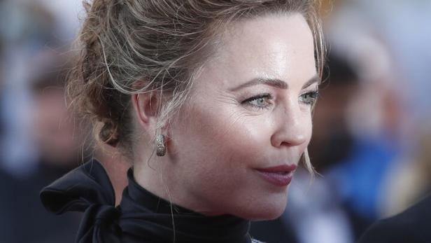 Melissa George mit hochgestecktem Haar trägt ein elegantes Kleid mit schwarzer Schleife und Perlenbesatz vor unscharfem Hintergrund.