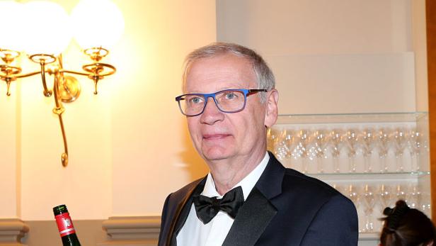 Günther Jauch im Smoking hält bei einem Empfang eine Weinflasche und ein gefülltes Glas in der Hand.