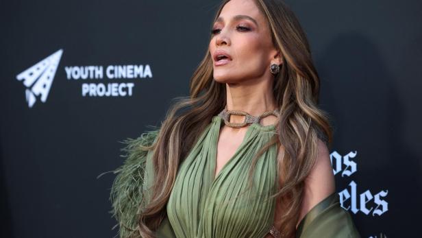 Jennifer Lopez trägt ein olivgrünes Kleid vor einer schwarzen Wand mit dem Logo des Youth Cinema Project.