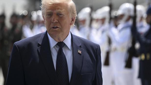 Donald Trump trägt einen dunklen Anzug vor einer Ehrenformation von Soldaten in weißen Uniformen.