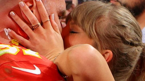 Taylor Swift küsst Travis Kelce, der ein rotes Trikot der Kansas City Chiefs trägt.