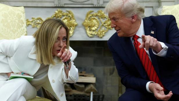 Giorgia Meloni und Donald Trump sitzen sich gegenüber und deuten gestikulierend aufeinander.