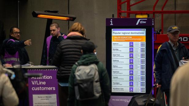 Bahnhofhalle mit V/Line-Informationsstand, Reisenden und Abfahrtsanzeige bei einer Störung.