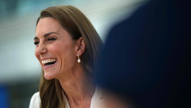 Prinzessin Kate lacht herzlich in einem hellen Oberteil mit Perlenohrringen.