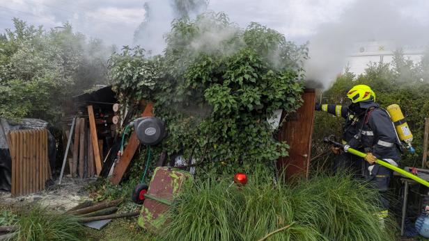 Feuerwehrmann löscht Rauch an einem stark bewachsenen Schuppen im Garten.