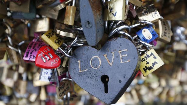 Viele Liebesschlösser, darunter ein herzförmiges mit der Aufschrift „Love“, hängen an einem Gitter.