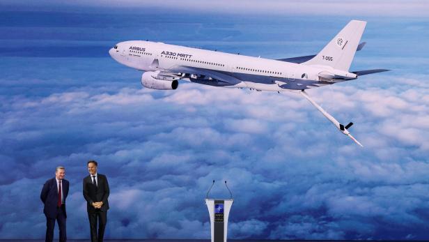 Zwei Männer vor NATO-Pult, darüber ein Airbus A330 MRTT über den Wolken.