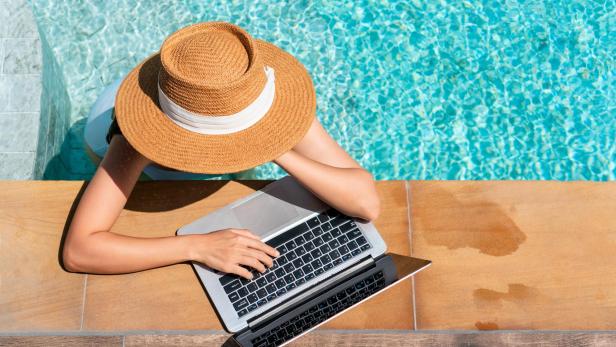 Eine Frau ist in einem Pool und trägt einen Sonnenhut und arbeitet an einem Laptop