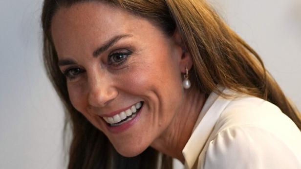 Prinzessin Kate lächelt freundlich in die Kamera und trägt eine weiße Bluse sowie Perlenohrringe.