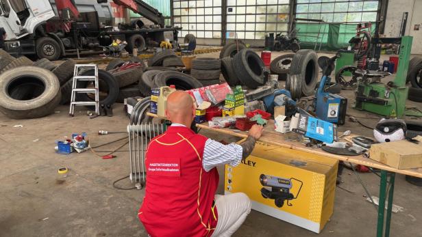 Ein Mann im roten Westen richtet in einer Werkhalle einen unordentlichen Reifen- und Lkw-Reparaturbereich ein.