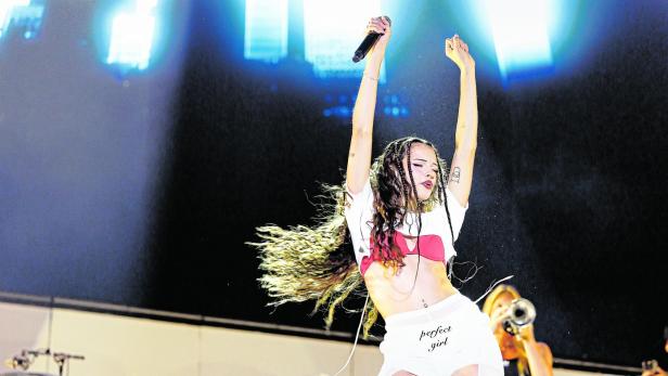 Nina Chuba mit Mikrofon und wehendem Haar performt auf einer Bühne vor einem hellen Hintergrund.