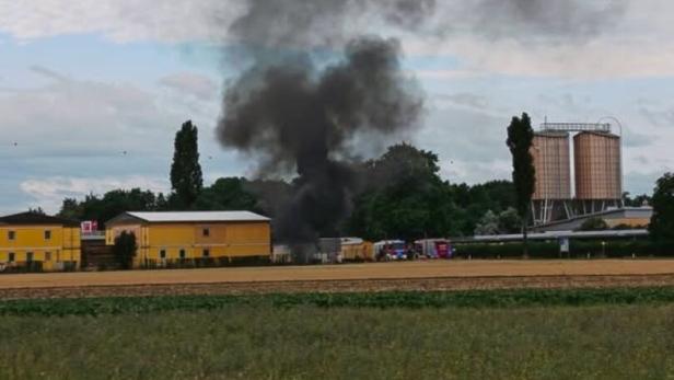 Dichter schwarzer Rauch steigt hinter Gebäuden auf, offenbar ein Brand auf einem Gelände im Grünen.