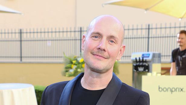 Oliver Petszokat alias Oli.P steht in schwarzem Anzug bei einem Event im Freien.