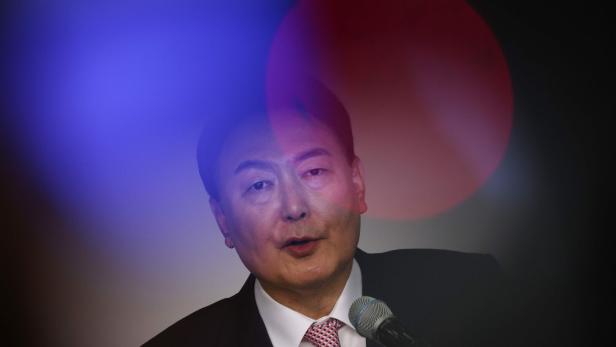 Der südkoreanische Präsident Yoon Suk-yeol spricht vor einem Mikrofon, umrahmt von abstrakten blauen und roten Lichteffekten.