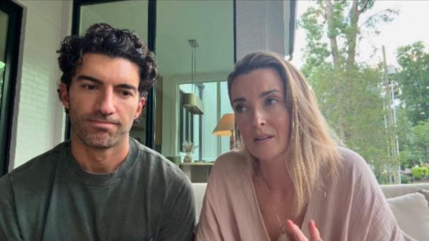 Justin Baldoni mit dunklen Locken und seine Emily Baldoni mit blondem Haar sitzen nebeneinander und sprechen in die Kamera.
