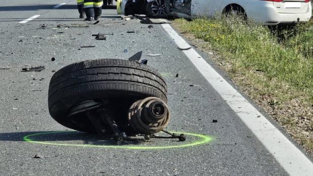 Schwerer Verkehrsunfall mit zerstörtem Auto, Feuerwehr, Trümmern und abgerissenem Rad auf der Straße.