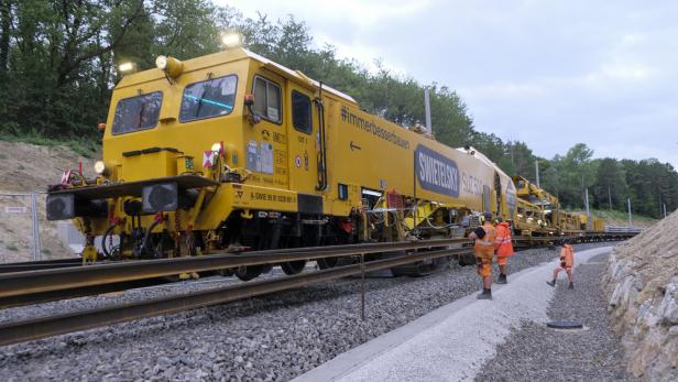 Gelbe Gleisbaumaschine mit Arbeitern auf einer Bahnstrecke im Wald.
