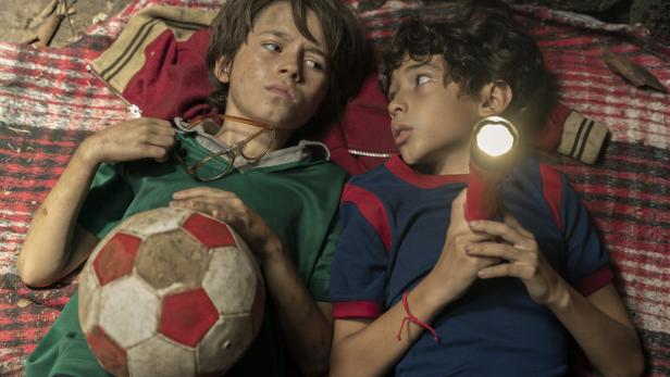 Zwei Jungen liegen auf einer Decke, einer hält einen Fußball und der andere eine Taschenlampe.