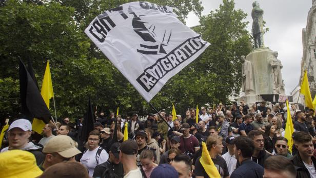 Menschenmenge bei einer Demonstration mit schwarzen und gelben Fahnen vor einem Denkmal.