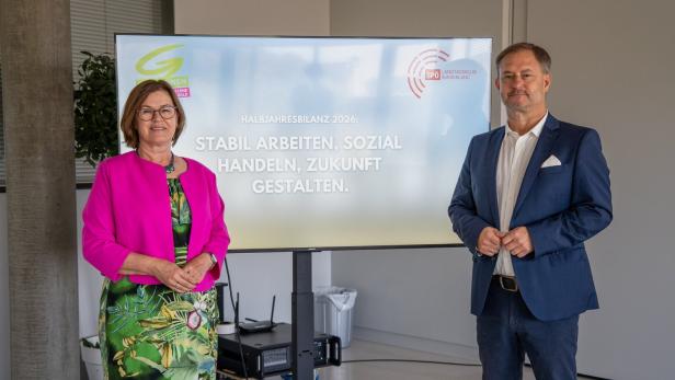 Zwei Politiker stehen vor einer Tafel mit der Aufschrift „Halbjahresbilanz 2026“.