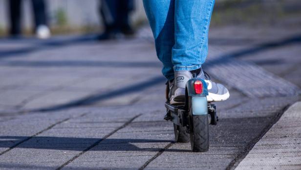 Person fährt auf einem E-Scooter über einen Gehweg.