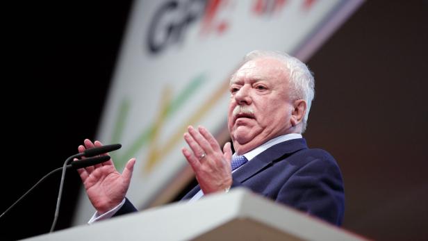 Ein Mann mit weißem Haar und Schnurrbart gestikuliert an einem Rednerpult.