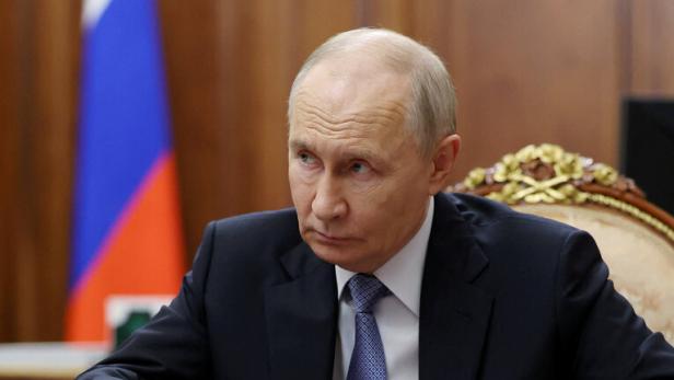 Wladimir Putin sitzt an einem Konferenztisch vor einer russischen Flagge und blickt auf Dokumente.