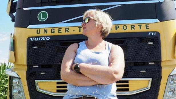 Eine Frau mit Sonnenbrille lehnt vor einem gelben Volvo-Lkw mit verschränkten Armen.