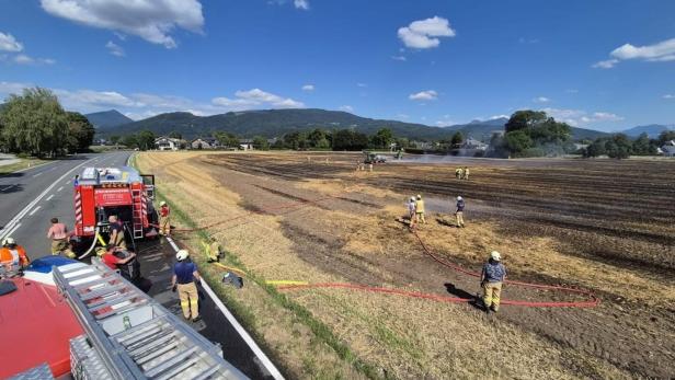 Feuerwehr löscht einen ausgebrannten Acker am Straßenrand mit mehreren Einsatzkräften und Fahrzeugen.