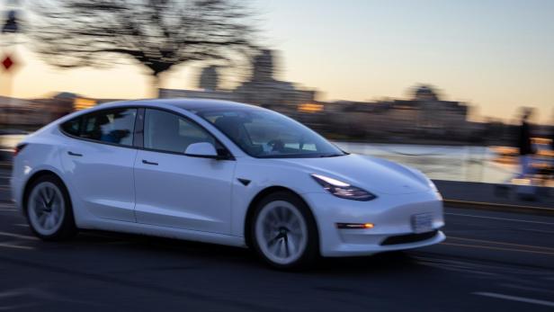 Weißer Tesla fährt bei Dämmerung auf einer Straße vorbei.