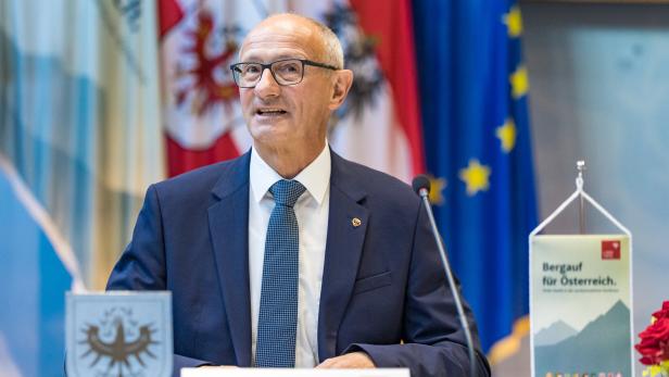 Anton Mattle spricht vor österreichischen und europäischen Flaggen an einem Pult mit der Aufschrift „Bergauf für Österreich“.