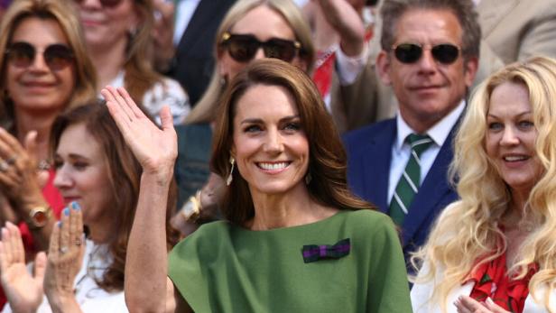 Prinzessin Kate winkt lächelnd in einem grünen Kleid in die Menge, während weitere Zuschauer im Hintergrund applaudieren.