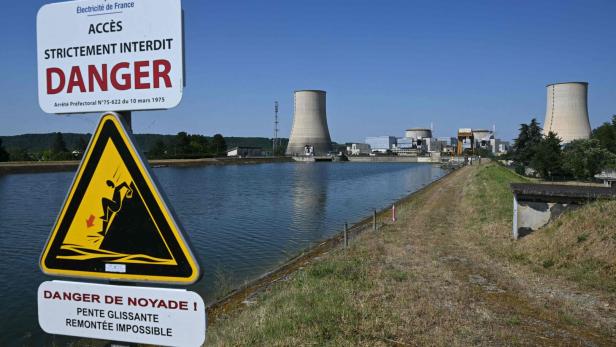 Warnschilder am Ufer vor einem Kernkraftwerk mit Kühltürmen.
