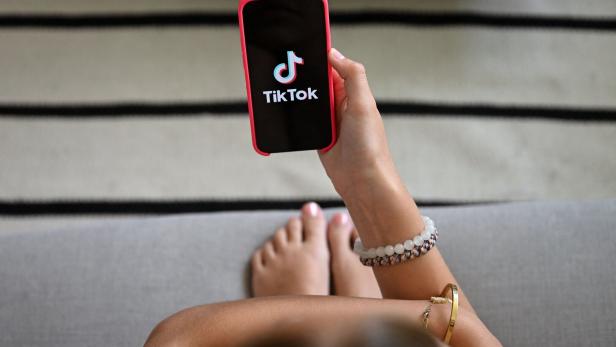 Eine Jugendliche schaut auf ihr Smartphone, auf dem das TikTok-Logo zu sehen ist. 