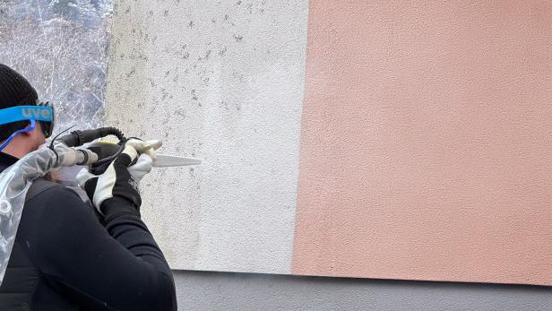 Person reinigt eine Hausfassade mit einem Trockeneisstrahlgerät.