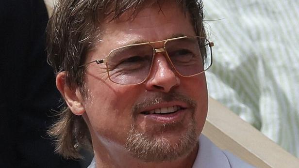 Brad Pitt trägt ein helles Hemd, eine goldene Halskette und eine Brille mit goldenem Rahmen.